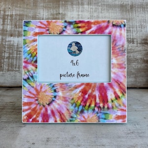 May include: A square 4x6 picture frame with a vibrant tie-dye pattern in shades of pink, orange, yellow, and blue. The frame has a light blue interior and features the text "4x6 picture frame". A small circular image of a bird is in the top center.
