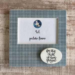 May include: A 4x6 picture frame with a blue plaid pattern. The frame has a white insert with a circular image of a bird and the words "4x6 picture frame". An oval accent piece reads "for this child we have prayed".