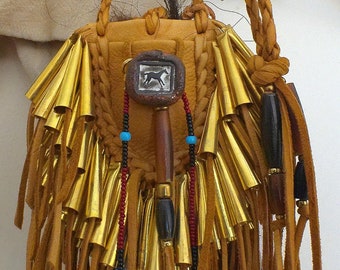 May include: A brown leather pouch with gold fringe and beads. The pouch has a braided leather strap and a small, decorative wooden handle. The pouch is decorated with a small, metal horse design.