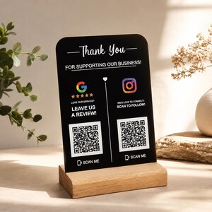 以下が含まれることがあります： 上部の角が丸い黒い長方形の看板。白い文字で「Thank You FOR SUPPORTING OUR BUSINESS」と書かれています。5つ星のGoogleロゴとInstagramロゴがあり、それぞれの下に「SCAN ME」と書かれたQRコードが配置されています。