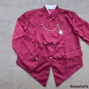 May include: A burgundy jacket with a white collar and gold buttons. The double-breasted jacket features a decorative chain and medallion. The jacket has a pocket on the right side and is made of a smooth fabric.