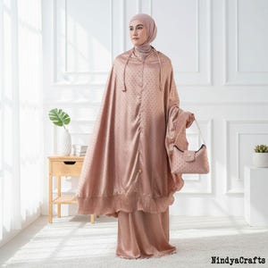 May include: A woman in a blush pink prayer outfit and matching handbag. The outfit features a head covering, a long cloak with a dotted pattern, and a skirt. The handbag has a chain strap and a flap closure.
