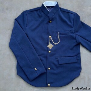 Pode incluir: Casaco azul marinho com gola mandarim e botões dourados. Uma corrente decorativa dourada com um medalhão é presa ao bolso. O casaco tem forro de gola branco e um bolso pequeno.