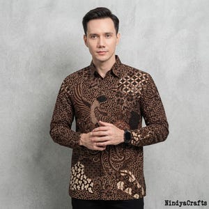 May include: A long-sleeved button-down shirt featuring a dark brown and tan batik pattern with intricate floral and geometric motifs. The shirt has a standard collar, a front button placket, and a black wristwatch on the left wrist.