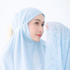 Può includere: Un abito da preghiera azzurro con copricapo abbinato. Il copricapo e l'abito sono rifiniti con delicate perline bianche. La manica presenta un design in pizzo dettagliato. L'abito è realizzato in un tessuto morbido e leggero.