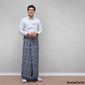 May include: A white long-sleeved button-down shirt with a black collar trim and a chest pocket, paired with a floor-length grey sarong featuring a repeating white and red diamond pattern with floral motifs. The text NindyaCrafts is in the corner.