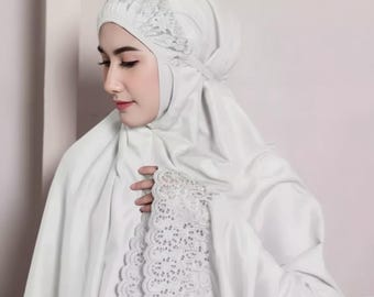 Op de afbeelding: Een witte gebedskleding set, inclusief een hoofdbedekking en een bijpassende sjaal. De hoofdbedekking heeft delicate kanten details. De set is gemaakt van een zachte, vloeiende stof.