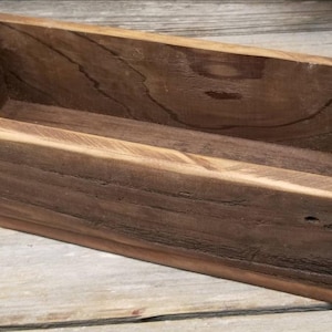 May include: A rustic wooden rectangular box with a natural brown finish. The box is made of reclaimed wood and has a distressed look. It is perfect for displaying small items or plants.