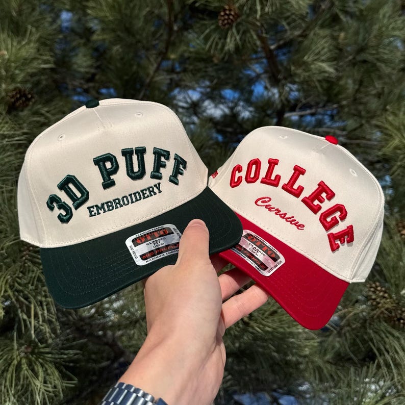 May include: Two baseball caps with embroidered text. One cap is cream-colored with a dark green brim and the words "3D PUFF EMBROIDERY" in dark green. The other cap is cream-colored with a red brim and the word "COLLEGE" in red.