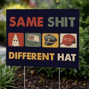 May include: A dark blue yard sign with the text "SAME SHIT DIFFERENT HAT" in orange, green, and yellow. The sign features four images of hats: a KKK hood, a Confederate hat, a military hat, and a "Make America Great Again" hat.