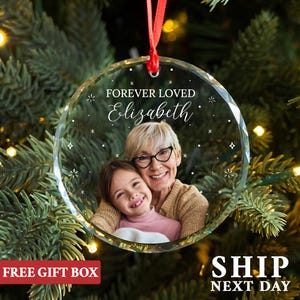 May include: A clear glass Christmas ornament with a photo of a woman and a child. The ornament has a white background with silver glitter stars and the text "FOREVER LOVED Elizabeth".