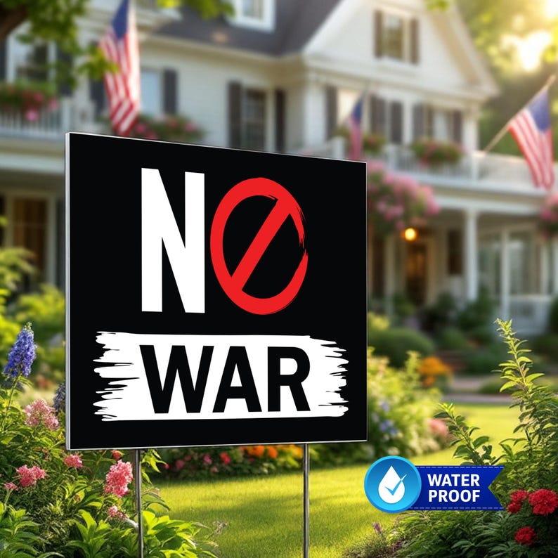 May include: Black yard sign with the words "NO WAR" in white, with a red circle and slash through the word "NO". The sign is in a garden with a house and American flags in the background.