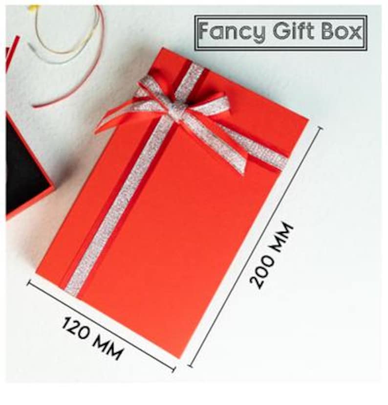 May include: A rectangular red gift box with a silver glitter ribbon bow on top. The box measures 200 mm by 120 mm. The text "Fancy Gift Box" is printed in a black rectangular frame at the top right corner of the image.