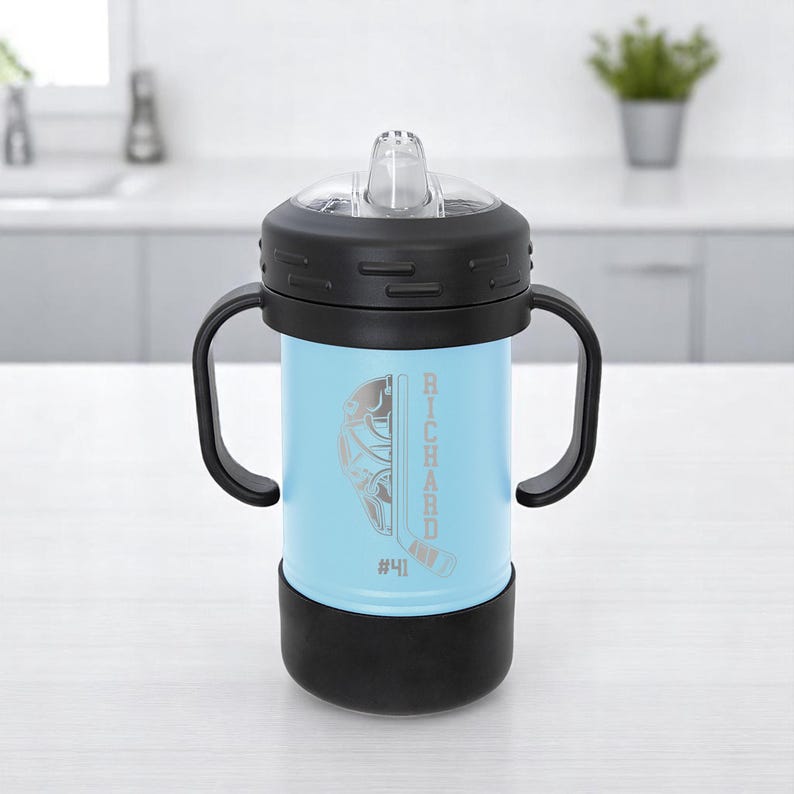 May include: A light blue sippy cup with a black lid, handles, and base. The cup features a hockey-themed design with the name "RICHARD" and the number "#41" etched on the side. The cup has a clear, flip-top spout.