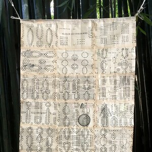 May include: A vintage, cream-colored paper sheet with black dots arranged in various patterns. The sheet is titled "Album de Esquemas" and is hanging from a string in a bamboo forest.