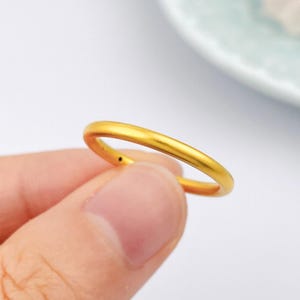 Op de afbeelding: Een eenvoudige, massief gouden ring met een gladde, matte afwerking en een afgerond bandprofiel. De ring heeft een uniforme, cirkelvormige vorm met een constante dikte over de gehele band, met een heldere, warme geelgouden metaalkleur.