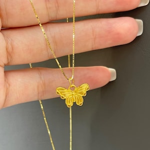 以下が含まれることがあります： 金色の蝶のペンダントネックレス。蝶のペンダントは精巧に作られており、繊細なチェーンから吊り下げられています。ネックレスはニュートラルな背景に表示されています。