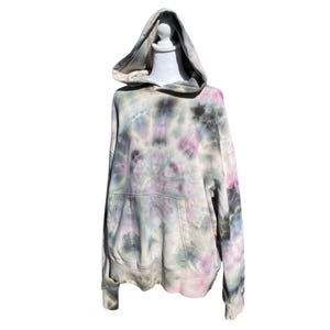 May include: A tie-dye hoodie in shades of grey, pink, and green. The hooded sweatshirt has a front pocket and is displayed on a white mannequin. The tie-dye pattern is a spiral design.
