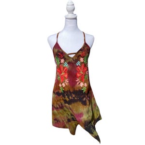 May include: A sleeveless dress with a tie-dye pattern in shades of brown, green, and pink. The dress features a V-neckline and is adorned with embroidered red and pink flowers with green leaves. The dress is displayed on a white mannequin.