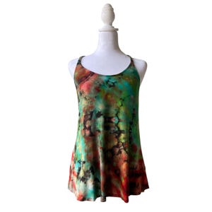 May include: A tie-dye vest top in shades of red, green, and black, displayed on a white mannequin. The sleeveless top has a scoop neck and a flowing, A-line silhouette. The fabric features a mottled pattern.