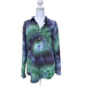 May include: A long-sleeved shirt with a tie-dye pattern in shades of green, blue, and purple. The shirt has a collared neckline, two chest pockets, and a button-down placket. The shirt is displayed on a white mannequin.