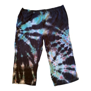 May include: Black tie-dye capri pants with a unique spiral pattern. The pants feature a mix of colors, including black, teal, and pink. The capris have a comfortable elastic waistband and side slits at the hem.