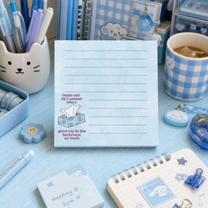 May include: A square light blue notepad with horizontal lines and a graphic of a tissue box. The text reads: turns out all I needed was a good cry in the bathroom at work. The paper has a subtle marbled texture and is centered in the frame.
