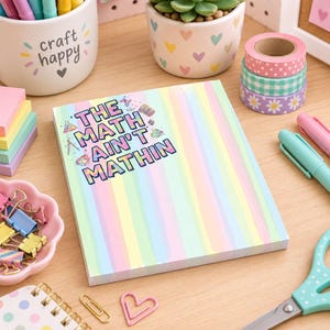 May include: A rectangular notepad with a pastel rainbow striped pattern and the text THE MATH AIN'T MATHIN printed in a colorful, blocky font. The notepad features small illustrations of math-related icons like calculators and geometric shapes.