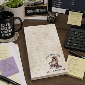May include: A rectangular notepad with horizontal lines and a vintage-style paper texture. The bottom features a graphic of a raccoon sitting in a wooden chair with the text: IT IS WHAT IT IS AND IT IS NOT GREAT printed in black capital letters.