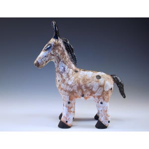 Pode incluir: Estatueta de burro de cerâmica artesanal. O burro é pintado com um padrão salpicado de manchas brancas, castanhas e pretas. A crina e a cauda são pretas. A estatueta tem um estilo de arte popular.