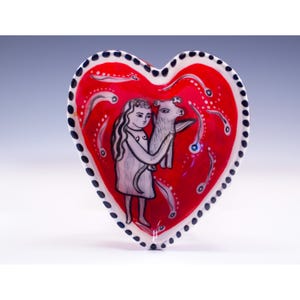 May include: A heart-shaped ceramic dish with a glossy red interior featuring a black and white illustration of a person holding a small dog. The rim is white with a repeating pattern of black dots, and the background is decorated with white swirls.