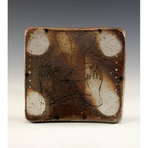 Puede incluir: Azulejo de cerámica cuadrado con una superficie veteada marrón y blanca. El azulejo presenta dos contornos de manos dibujadas a mano conectados por líneas de puntos. Cuatro formas circulares blancas están en las esquinas.