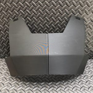 May include: Two-piece, dark gray plastic component with a geometric design. The pieces are rectangular with angled edges and a notched top. The object is likely a part of a larger product or device.