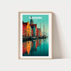 Puede incluir: Lámina artística enmarcada que representa Flensburgo, Alemania. La ilustración muestra edificios coloridos reflejados en el agua, con veleros y el texto "FLENSBURG GERMANY". La impresión está en un marco de madera clara.