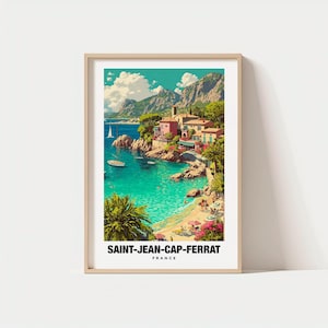 May include: A framed art print of Saint-Jean-Cap-Ferrat, France. The image depicts a coastal scene with turquoise water, boats, and colorful buildings. The print has a light wood frame and the text "SAINT-JEAN-CAP-FERRAT FRANCE" at the bottom.
