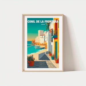 May include: A framed art print featuring a coastal scene with the text "CONIL DE LA FRONTERA SPAIN." The artwork depicts white buildings, a turquoise sea, and a sandy beach. Potted plants and colorful buildings add vibrancy to the scene.