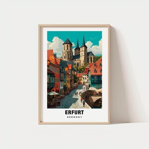 May include: A framed art print featuring a colorful street scene in Erfurt, Germany. The artwork depicts a cobblestone street lined with buildings in shades of orange, red, and green, leading to a church with tall spires. The text "ERFURT GERMANY" is at the bottom.