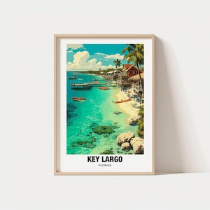 Op de afbeelding: Een ingelijste print met een levendige kustscène van Key Largo, Florida. Het kunstwerk toont een turquoise oceaan, een zandstrand en gebouwen met rode daken. Palmbomen en boten zijn ook zichtbaar, met de tekst "KEY LARGO FLORIDA" onderaan.