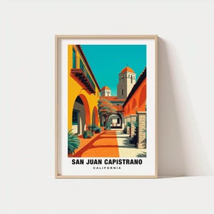 May include: A framed art print featuring a vibrant illustration of San Juan Capistrano, California. The artwork showcases a courtyard with orange arches, a red-tiled roof, and a turquoise sky. The text "SAN JUAN CAPISTRANO CALIFORNIA" is at the bottom.