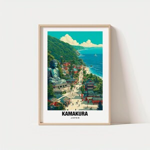 以下が含まれることがあります： 日本の鎌倉の風景を描いた額入りアートプリント。大きな座像の仏像、伝統的な日本の建物、ターコイズブルーの海とヨットのある海岸の風景が描かれています。「KAMAKURA JAPAN」の文字が下部にあります。