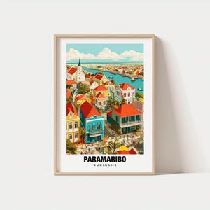 Op de afbeelding: Een ingelijste kunstdruk met een kleurrijke illustratie van Paramaribo, Suriname. Het kunstwerk toont levendige gebouwen met rode, gele en blauwe gevels, een kerk en een rivier met boten onder een blauwe lucht. De tekst "PARAMARIBO SURINAME" staat onderaan.