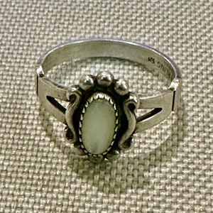 May include: A silver ring with a white oval-shaped stone set in a decorative silver design. The ring is marked "STERLING".