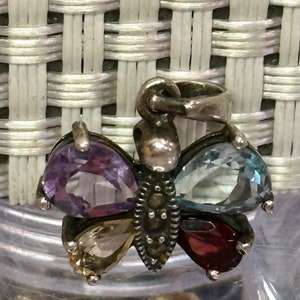 May include: A silver butterfly pendant with four gemstone wings. The wings are amethyst, aquamarine, topaz, and garnet.