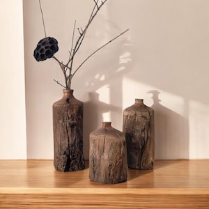 May include: Three rustic wooden vases, two of which are empty and one with a dried flower arrangement. The vases are all different sizes and shapes, and they have a natural, weathered look.