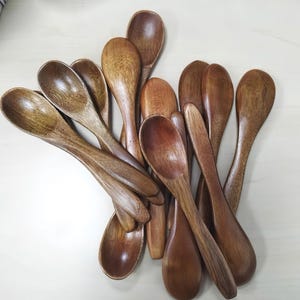 Może przedstawiać: Kolekcja drewnianych łyżek w różnych odcieniach brązu. Łyżki ułożone są w lekko zachodzącym na siebie wzorze, ukazując ich gładkie, wypolerowane powierzchnie. Łyżki wykonane są z naturalnego drewna.