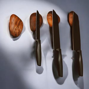 Puede incluir: Tres cuchillos de cocina negros con mangos de madera están montados en una pared con soportes magnéticos de madera.