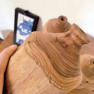 May include: Two wooden vases with a natural wood grain finish. The vases are made from a single piece of wood and have a unique, organic shape.