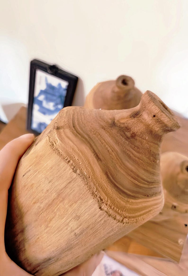 May include: Two wooden vases with a natural wood grain finish. The vases are made from a single piece of wood and have a unique, organic shape.