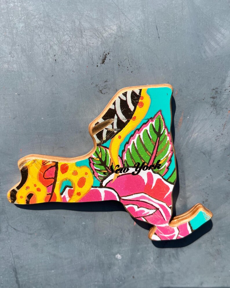 May include: A wooden New York state-shaped decorative item with a vibrant floral design. The artwork features a pink rose, green leaves, and yellow and orange patterns, with the words "New York" in cursive.