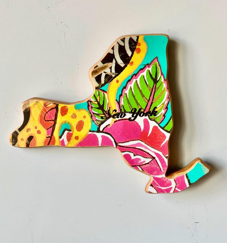May include: Wooden New York state cutout with a vibrant floral design. The artwork features a mix of colors, including pink, yellow, green, and teal. The words "New York" are written in black script across the design.